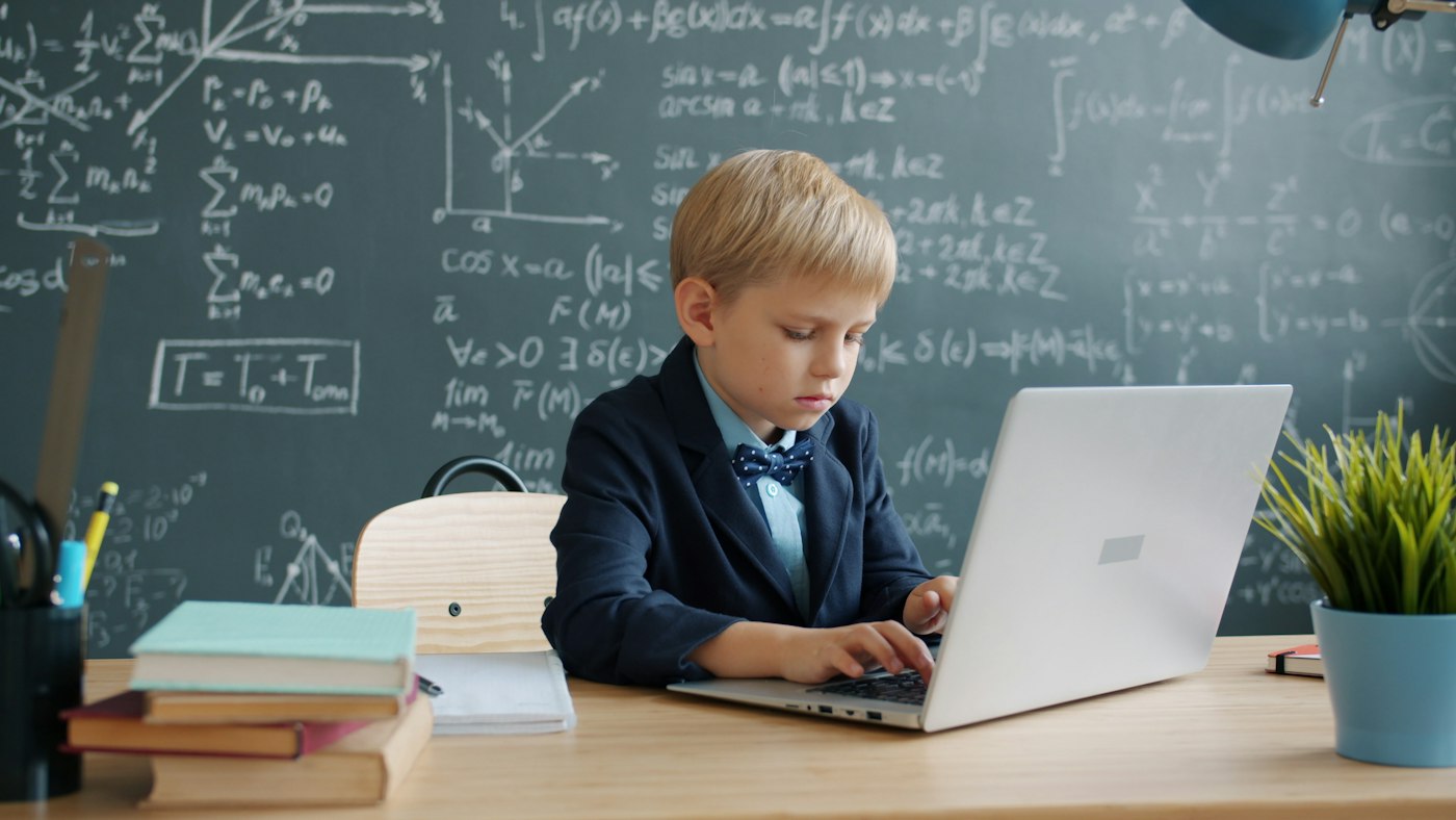 A boy working on a laptop in front of a chalkboard