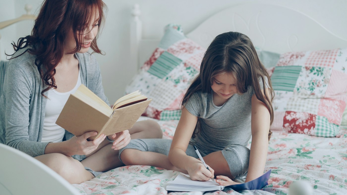 A mother reading while her daughter does homework beside her